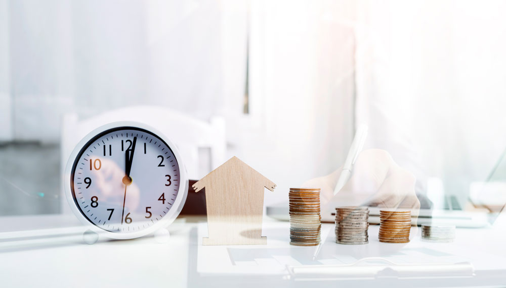 Wohnung verkaufen Frankfurt – Symbolbild mit Uhr, Münzstapeln und Holzhaus für Verkaufsdauer und Immobilienbewertung